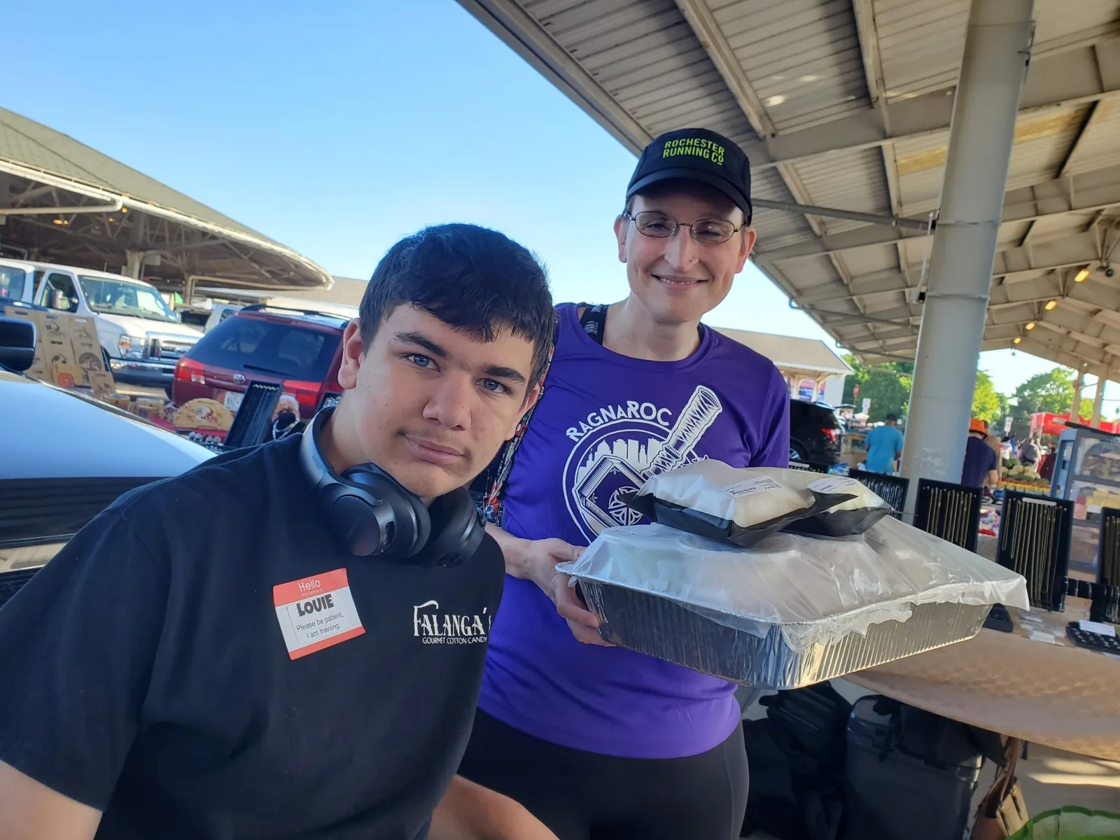 Louie in his Falanga's shirt with a customer picking up a tray of cotton candy at the Rochester Public Market
