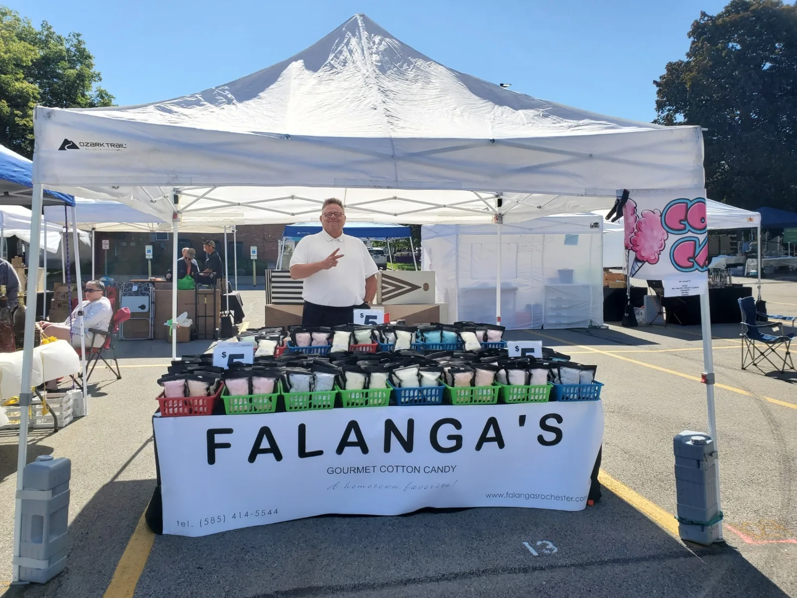 Vendor posing behind a full table of pre-bagged cotton candy at an outdoor market