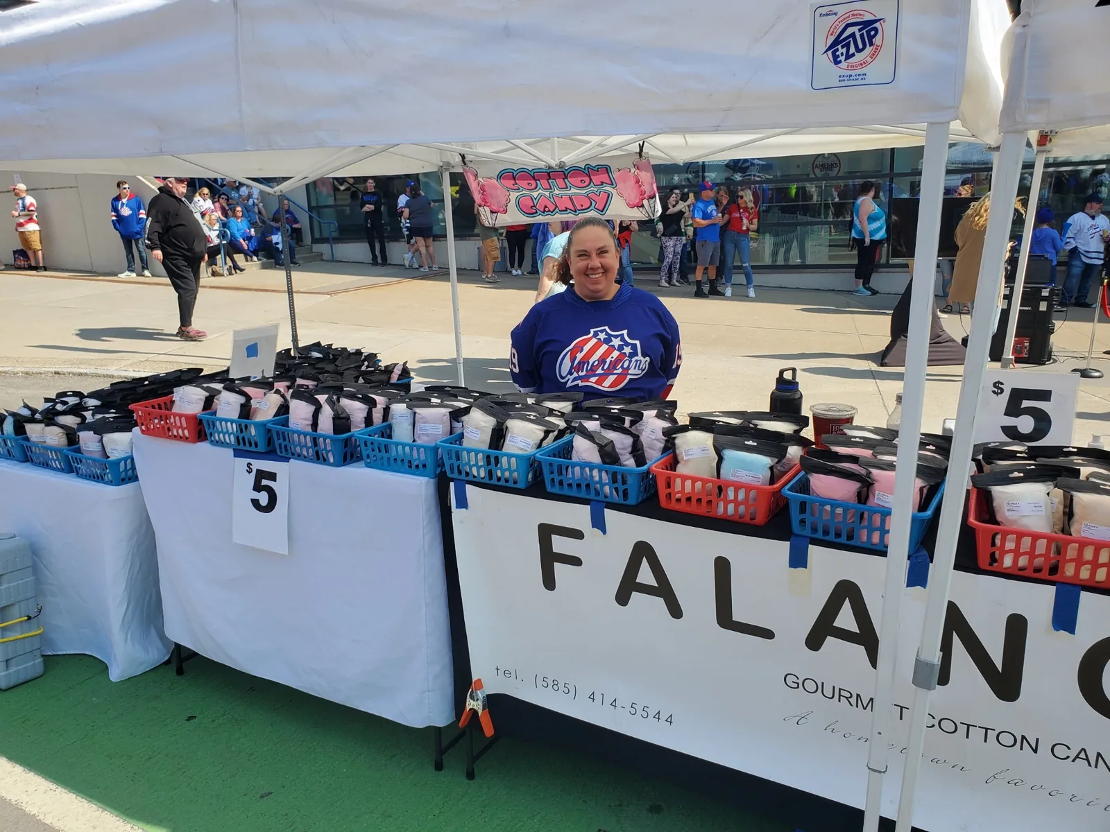 Jenny in an Amerks jersey smiling behind the Falanga's booth outside the arena